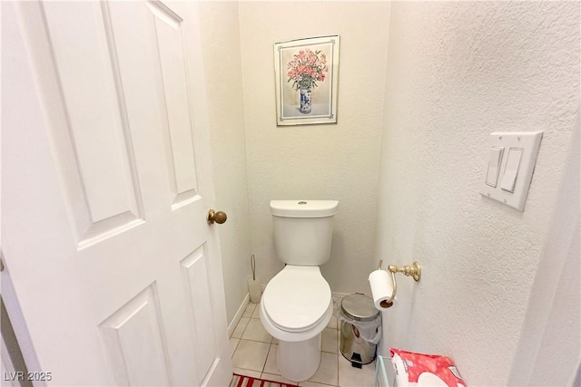 bathroom with toilet, tile patterned floors, a textured wall, and baseboards
