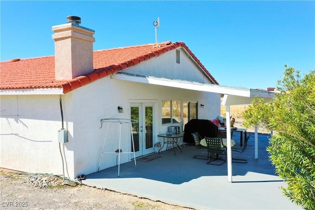 back of property featuring a patio, stucco siding, a chimney, french doors, and a tile roof