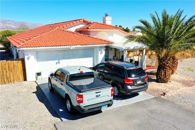 view of front of property featuring a tiled roof, stucco siding, fence, a chimney, and a garage