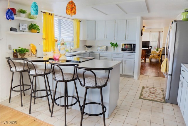 kitchen with a kitchen breakfast bar, a peninsula, light tile patterned flooring, stainless steel appliances, and a sink