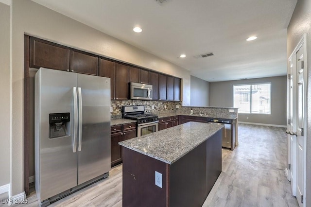 4516 Townwall St, Las Vegas, NV 89115 - kitchen with light stone counters, dark brown cabinetry, a kitchen island, tasteful backsplash, and appliances with stainless steel finishes