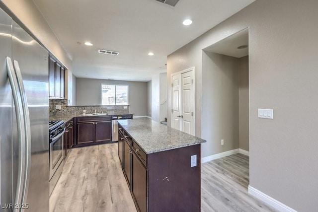 4516 Townwall St, Las Vegas, NV 89115 - kitchen featuring light wood finished floors, baseboards, light stone countertops, dark brown cabinets, and appliances with stainless steel finishes