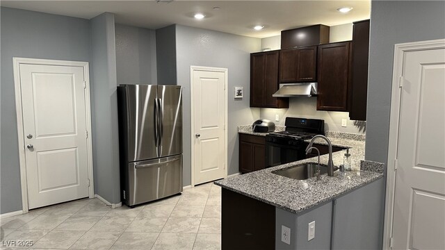 kitchen featuring black range with gas cooktop, under cabinet range hood, a sink, light stone counters, and freestanding refrigerator