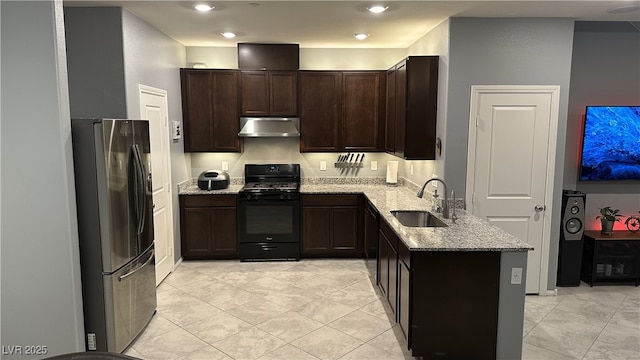 kitchen featuring black gas range oven, a sink, freestanding refrigerator, light stone countertops, and exhaust hood