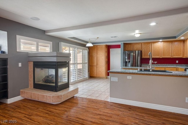 506 Staghorn Pass Ave, Las Vegas, NV 89183 - kitchen featuring stainless steel refrigerator with ice dispenser, a sink, a tiled fireplace, a raised ceiling, and light wood finished floors
