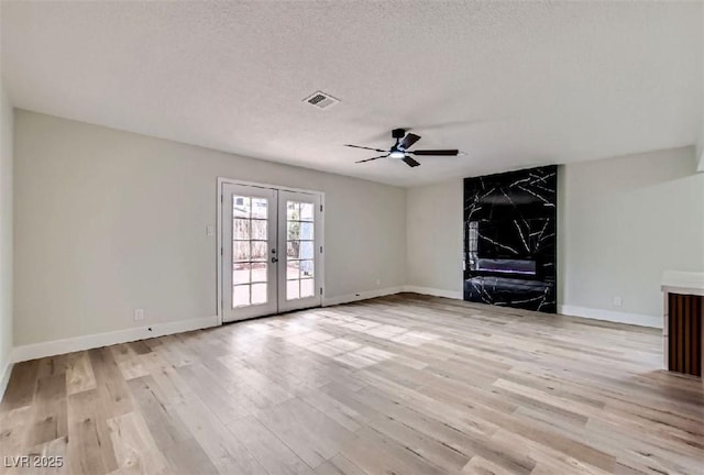 unfurnished living room with light wood finished floors, ceiling fan, french doors, and a textured ceiling