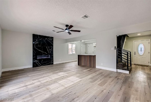 unfurnished living room with stairs, light wood-type flooring, visible vents, a high end fireplace, and a ceiling fan