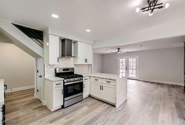 kitchen featuring wall chimney range hood, a peninsula, stainless steel gas range, and white cabinetry
