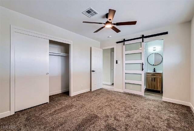 unfurnished bedroom featuring carpet, baseboards, a barn door, visible vents, and a closet