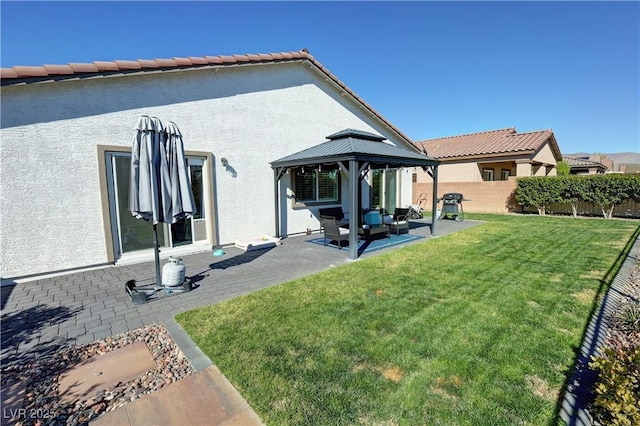 rear view of property with fence, a gazebo, stucco siding, a yard, and a patio area