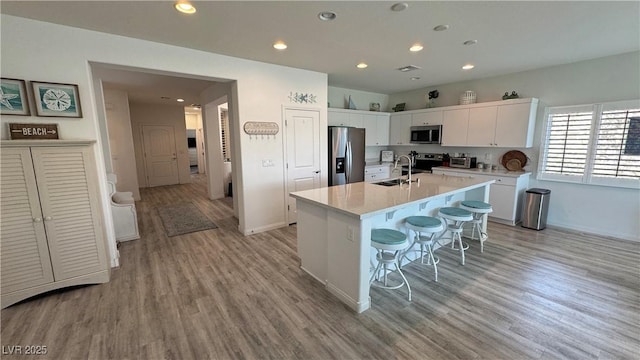 kitchen featuring light countertops, light wood-style flooring, a kitchen bar, stainless steel appliances, and white cabinetry