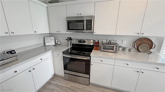 kitchen with light wood-style flooring, a toaster, light stone counters, white cabinets, and appliances with stainless steel finishes