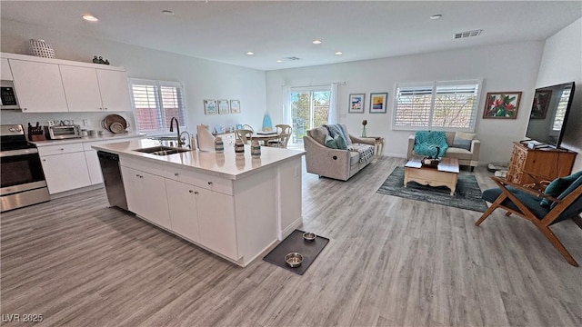 kitchen featuring open floor plan, a sink, light wood-type flooring, and appliances with stainless steel finishes