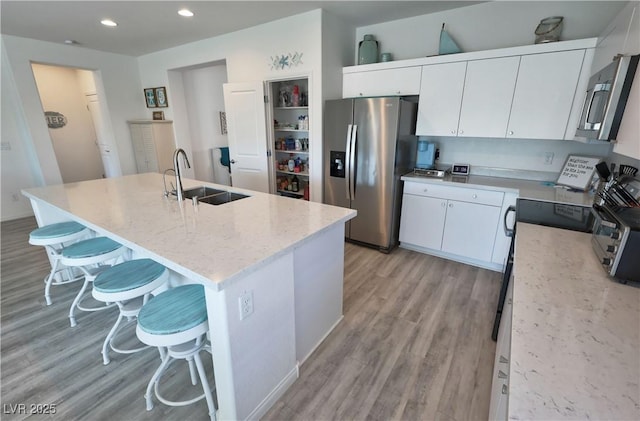 kitchen with a sink, light wood finished floors, white cabinetry, a breakfast bar, and stainless steel appliances