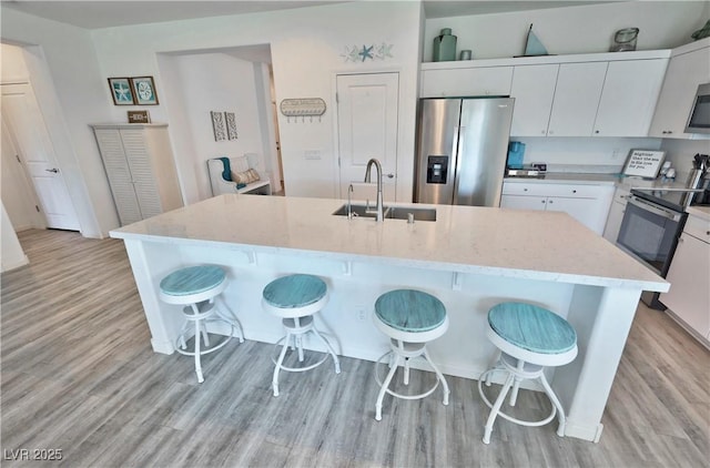kitchen featuring light wood-style flooring, a sink, a kitchen breakfast bar, and appliances with stainless steel finishes