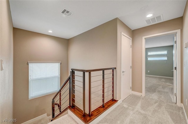 hall with visible vents, baseboards, an upstairs landing, and carpet floors