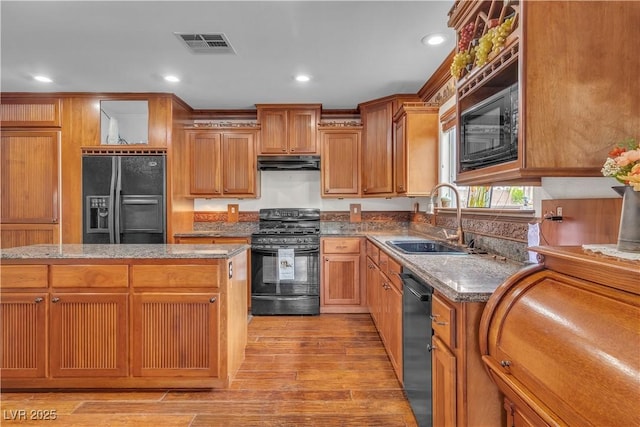 5050 Secret Rock St, Las Vegas, NV 89122 - kitchen featuring black appliances, under cabinet range hood, light stone countertops, light wood-type flooring, and brown cabinetry