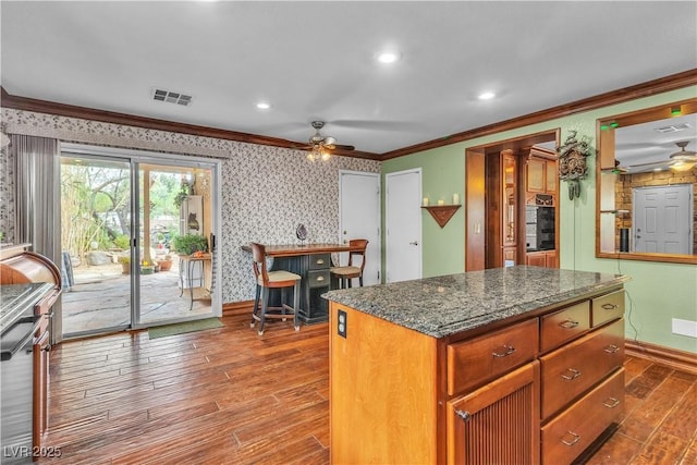 5050 Secret Rock St, Las Vegas, NV 89122 - kitchen featuring a ceiling fan, ornamental molding, wood-type flooring, a center island, and dark stone counters