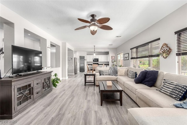 living room featuring baseboards, a ceiling fan, light wood-style flooring, and visible vents