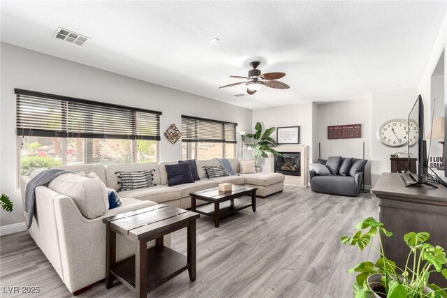 living room featuring visible vents, baseboards, ceiling fan, and light wood-type flooring