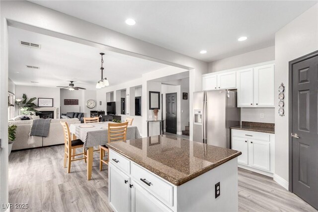 kitchen with a kitchen island, a ceiling fan, stainless steel refrigerator with ice dispenser, dark stone counters, and light wood-style flooring