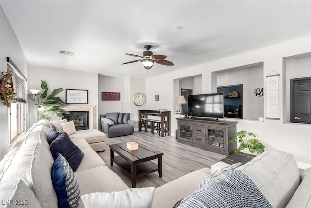 living room featuring ceiling fan, a glass covered fireplace, baseboards, wood finished floors, and visible vents