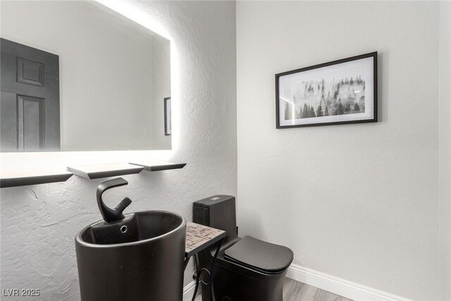 half bathroom featuring baseboards, a textured wall, toilet, and wood finished floors