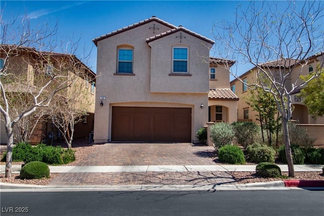 mediterranean / spanish home with a tile roof, a garage, decorative driveway, and stucco siding