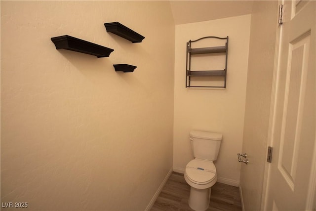 bathroom featuring baseboards, wood finished floors, and toilet