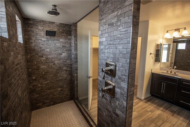 bathroom with a tile shower, vanity, and wood finished floors
