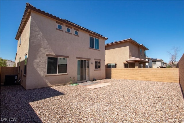 rear view of house with stucco siding, central AC unit, and a fenced backyard