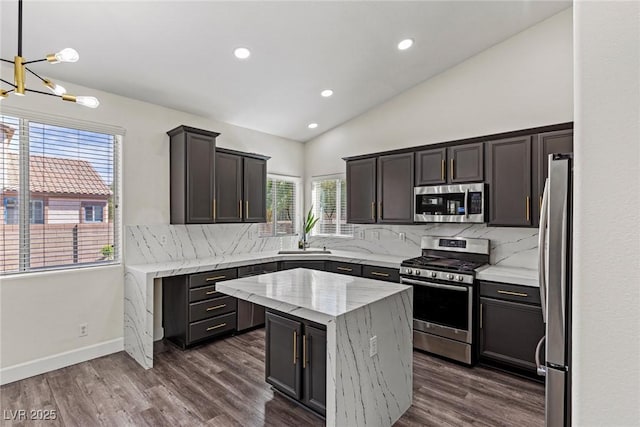 kitchen with dark wood-style flooring, appliances with stainless steel finishes, lofted ceiling, an inviting chandelier, and backsplash