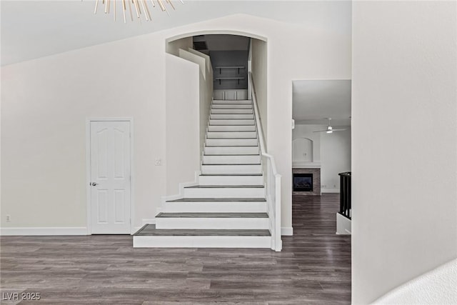 stairway with a fireplace, ceiling fan, wood finished floors, and arched walkways