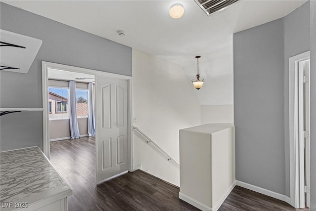 corridor featuring dark wood finished floors, baseboards, visible vents, and an upstairs landing