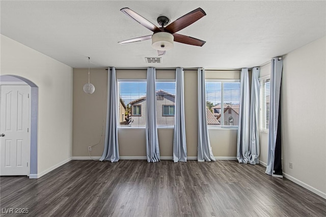 unfurnished room featuring visible vents, baseboards, a ceiling fan, dark wood finished floors, and arched walkways