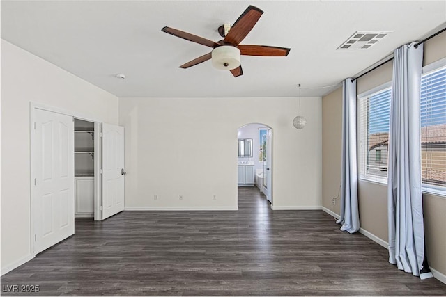empty room with arched walkways, dark wood-style floors, ceiling fan, and visible vents