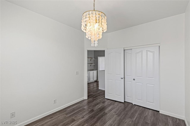 unfurnished bedroom with a closet, a notable chandelier, dark wood-style floors, and baseboards