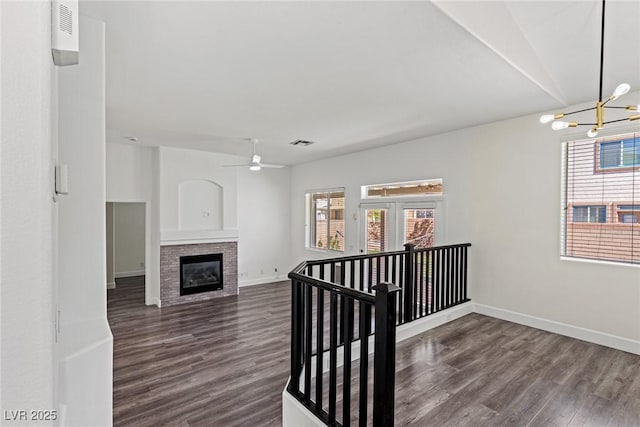 interior space featuring baseboards, wood finished floors, ceiling fan with notable chandelier, and a glass covered fireplace