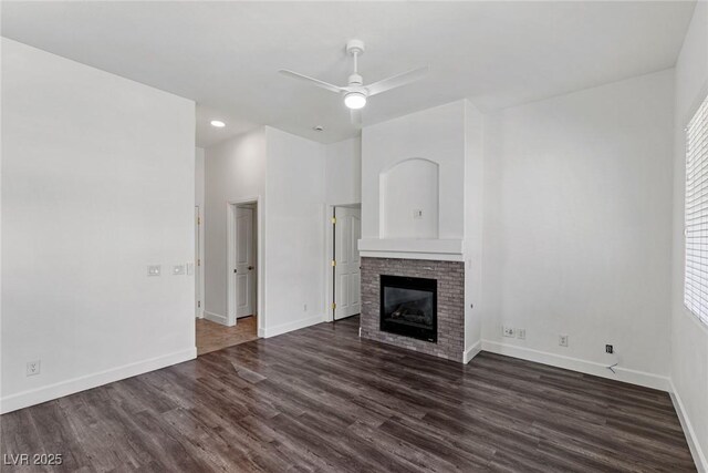 unfurnished living room with baseboards, ceiling fan, dark wood-type flooring, and a glass covered fireplace