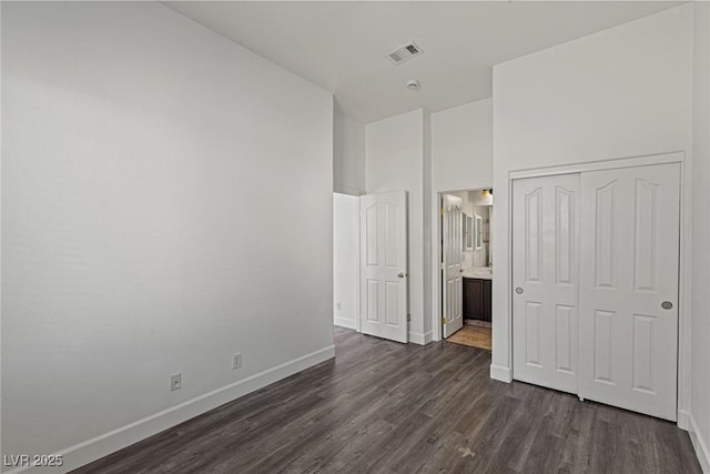 unfurnished bedroom featuring a closet, baseboards, dark wood finished floors, visible vents, and ensuite bathroom