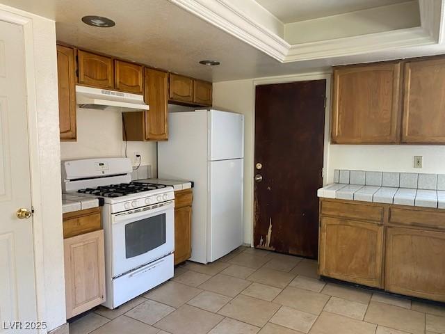 7732 Blackbird Ave, Las Vegas, NV 89145 - kitchen featuring white appliances, under cabinet range hood, tile countertops, a tray ceiling, and brown cabinetry