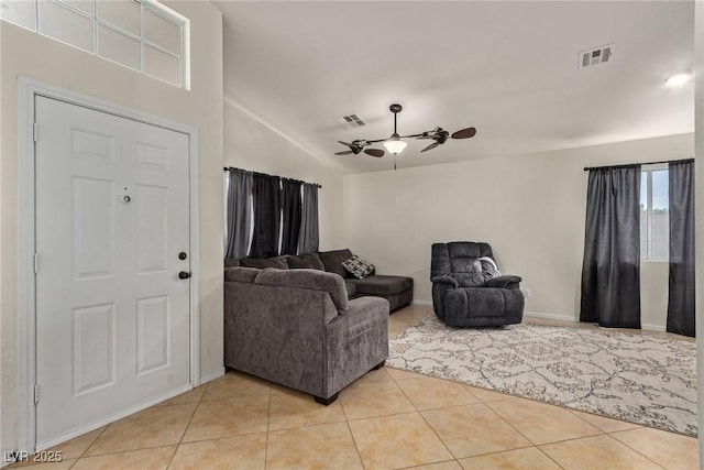 living area featuring ceiling fan, vaulted ceiling, visible vents, light tile patterned flooring, and baseboards