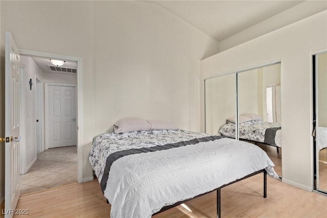 bedroom with light wood-style floors, high vaulted ceiling, a closet, visible vents, and baseboards
