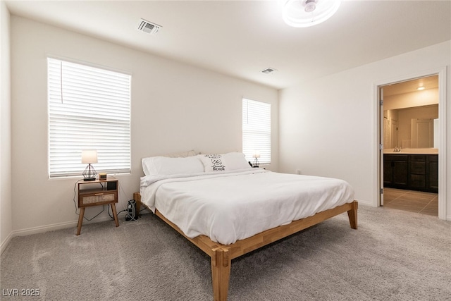 bedroom with visible vents, light colored carpet, baseboards, and connected bathroom