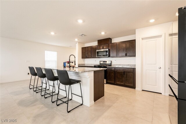 kitchen with an island with sink, a kitchen breakfast bar, dark brown cabinets, a sink, and stainless steel appliances