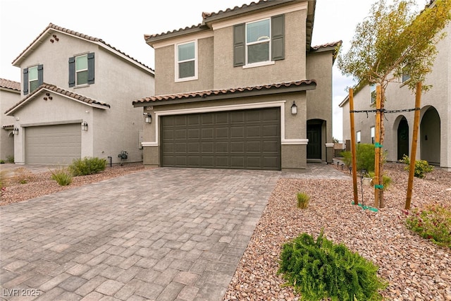 mediterranean / spanish home featuring a garage, driveway, stucco siding, and a tiled roof