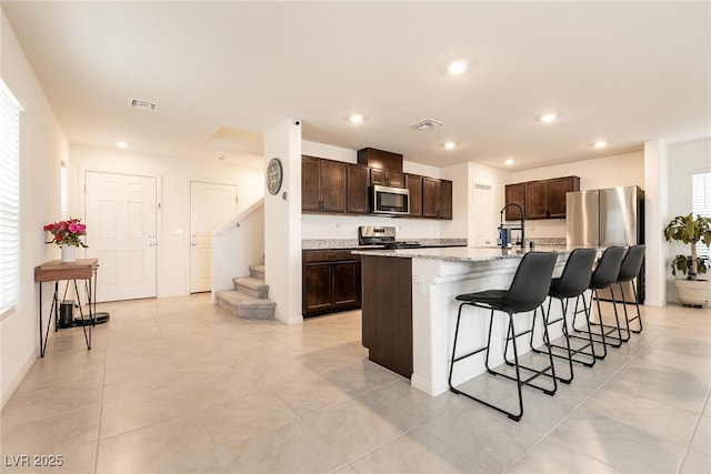 kitchen featuring dark brown cabinetry, a kitchen breakfast bar, visible vents, and stainless steel appliances