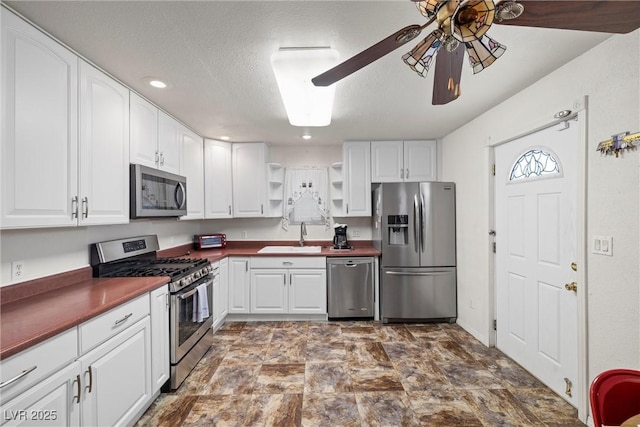 kitchen with a sink, open shelves, stainless steel appliances, dark countertops, and ceiling fan