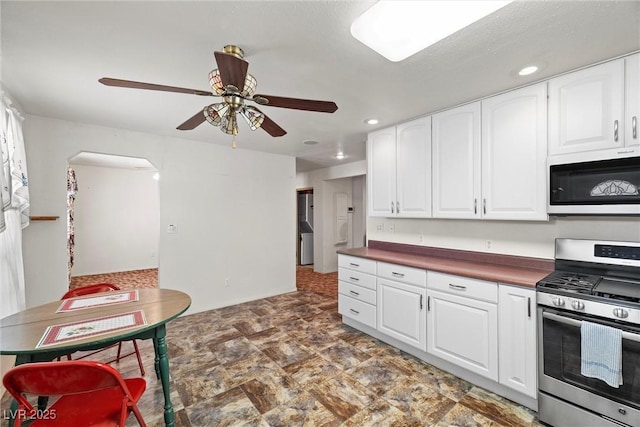 kitchen with stainless steel gas range oven, arched walkways, dark countertops, ceiling fan, and white cabinets