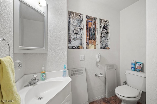 bathroom featuring baseboards, a textured wall, toilet, and vanity
